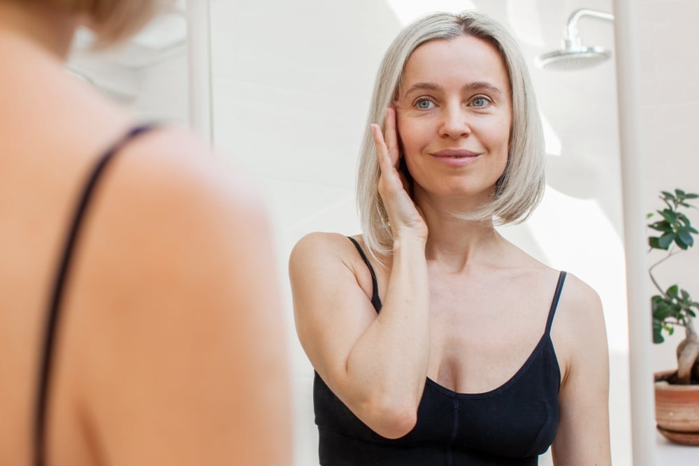 Woman examining her skin in the mirror, representing preventative Botox® and early wrinkle treatment. Woman examining her skin in the mirror, representing preventative Botox® and early wrinkle treatment.